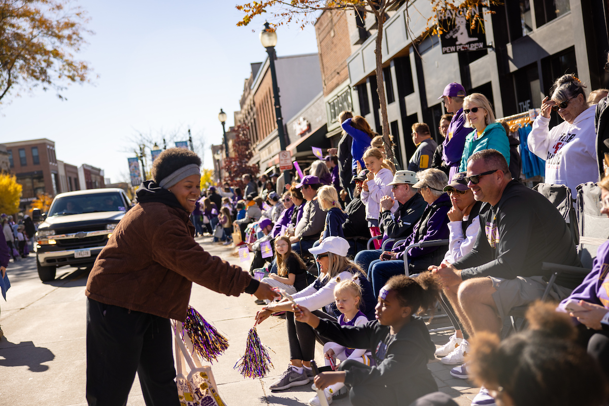 Woman in UNI Homecoming parade hands out pom-poms to parade goers
